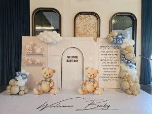 אולם לברית בירושלים בעיצוב חגיגי לתינוק, עם בלונים בצבעי שמנת ותכלת, דובוני קישוט ושלט "Welcome Baby Boy" באווירה מרגשת
