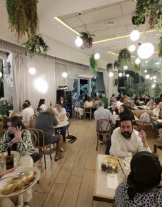 סועדים במסעדה חלבית כשרה בירושלים, באולם מעוצב עם צמחייה תלויה, תאורה חמה ואווירה מזמינה – חלק מהחוויה במסעדות כשרות בירושלים חלבי
